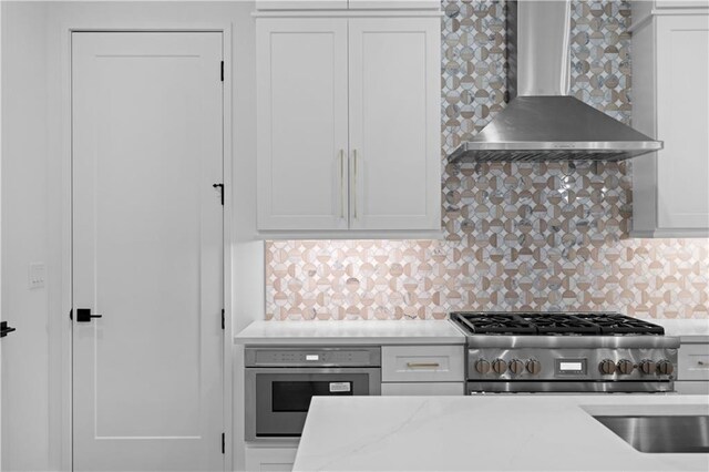 kitchen with sink, wall chimney exhaust hood, tasteful backsplash, white cabinets, and appliances with stainless steel finishes