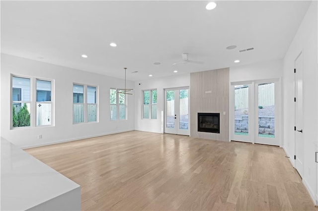 unfurnished living room featuring a large fireplace, ceiling fan, french doors, and light hardwood / wood-style floors