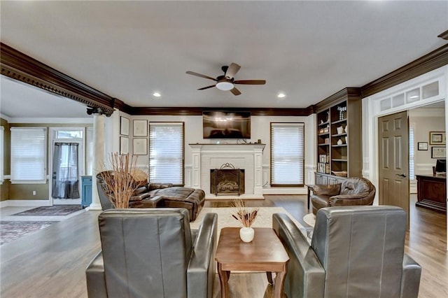 living room with built in features, hardwood / wood-style flooring, ceiling fan, and ornamental molding