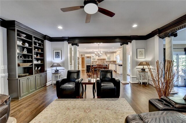 living room featuring light wood-type flooring, built in shelves, ceiling fan with notable chandelier, and crown molding