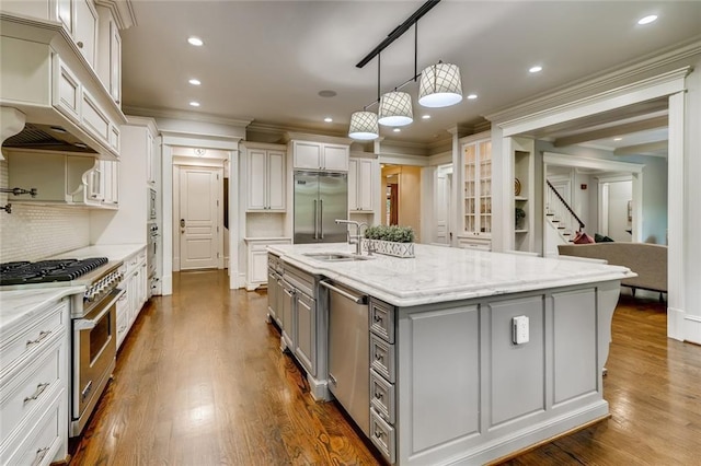 kitchen featuring hardwood / wood-style floors, premium range hood, decorative light fixtures, premium appliances, and a center island with sink