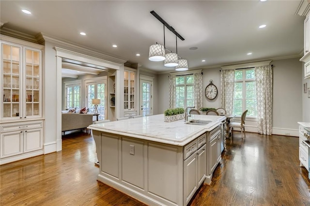 kitchen with pendant lighting, sink, dark hardwood / wood-style flooring, ornamental molding, and a center island with sink