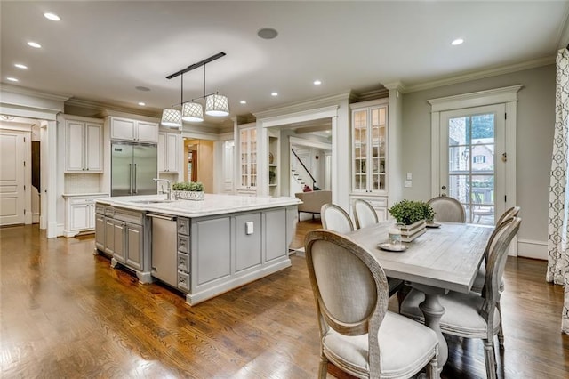 kitchen with hanging light fixtures, an island with sink, dark hardwood / wood-style flooring, built in fridge, and ornamental molding