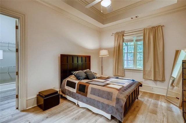 bedroom featuring light hardwood / wood-style floors, ceiling fan, a closet, a tray ceiling, and a spacious closet