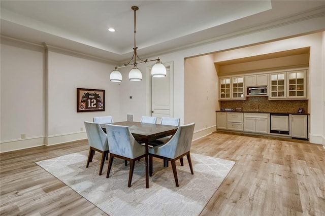 dining space featuring an inviting chandelier, light hardwood / wood-style floors, a raised ceiling, and sink