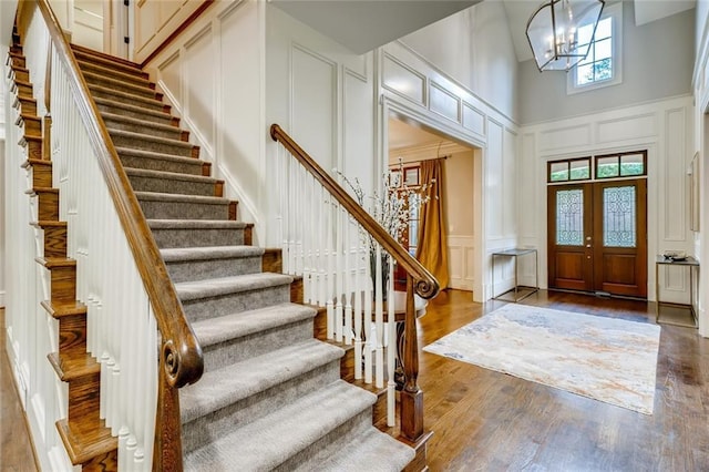 foyer with french doors, hardwood / wood-style floors, a towering ceiling, and an inviting chandelier