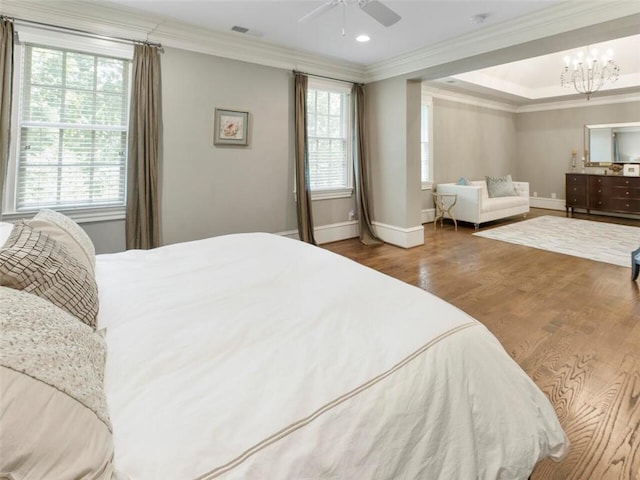 bedroom with crown molding, hardwood / wood-style floors, ceiling fan with notable chandelier, and a raised ceiling