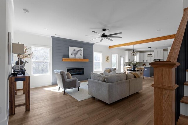 living room with a fireplace, beam ceiling, wood finished floors, and ceiling fan
