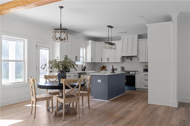 kitchen with stainless steel electric range oven, premium range hood, decorative backsplash, light countertops, and a center island