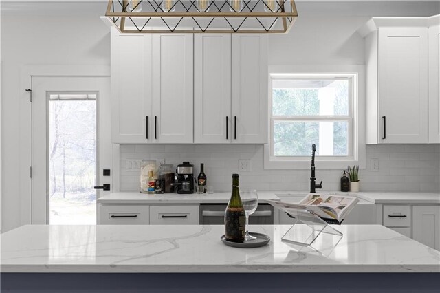kitchen with light stone countertops, dishwasher, decorative backsplash, white cabinets, and a sink