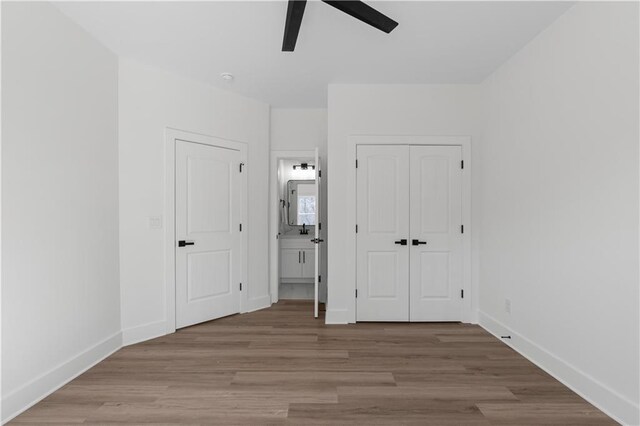 unfurnished bedroom featuring a closet, baseboards, ensuite bath, and wood finished floors