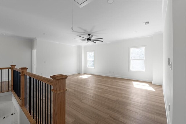 empty room featuring light wood finished floors, crown molding, baseboards, ceiling fan, and attic access
