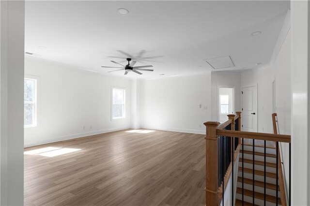 spare room featuring attic access, a ceiling fan, baseboards, and wood finished floors