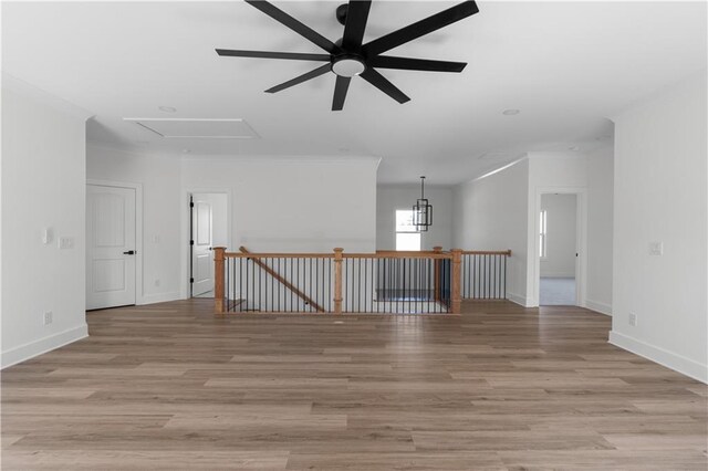empty room featuring baseboards, attic access, ceiling fan, crown molding, and light wood-type flooring