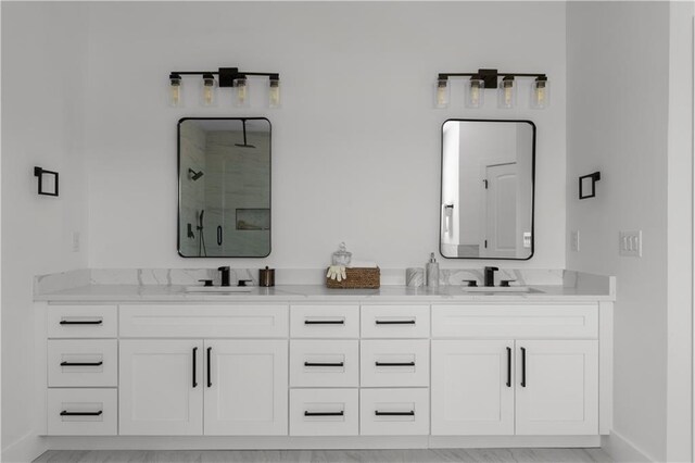 bathroom with a shower stall, double vanity, baseboards, and a sink