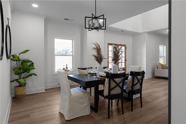 dining area with a notable chandelier, plenty of natural light, crown molding, and wood finished floors