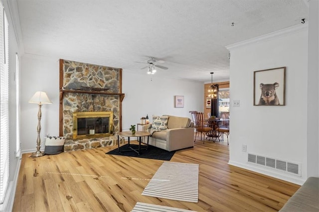 living room with ornamental molding, a textured ceiling, ceiling fan, hardwood / wood-style flooring, and a fireplace