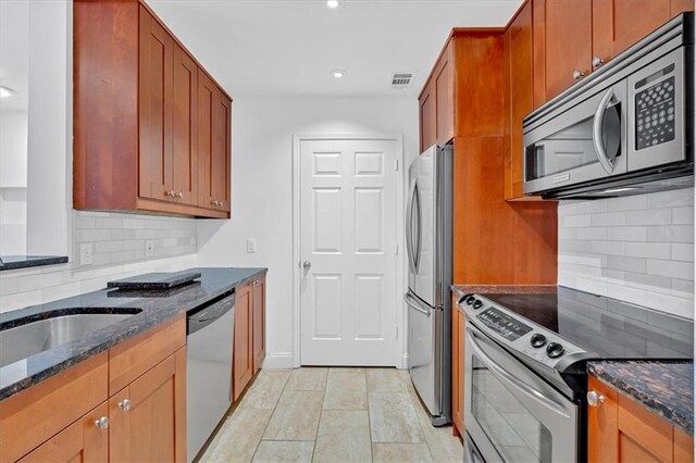 kitchen featuring appliances with stainless steel finishes, tasteful backsplash, sink, dark stone countertops, and light hardwood / wood-style flooring