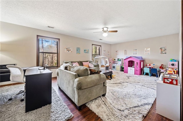 living area featuring dark wood-type flooring, a ceiling fan, visible vents, and a wealth of natural light