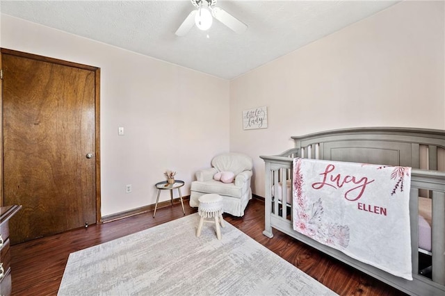 bedroom featuring baseboards, a crib, ceiling fan, and wood finished floors