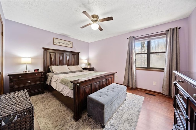 bedroom featuring a ceiling fan, baseboards, visible vents, light wood-style floors, and a textured ceiling