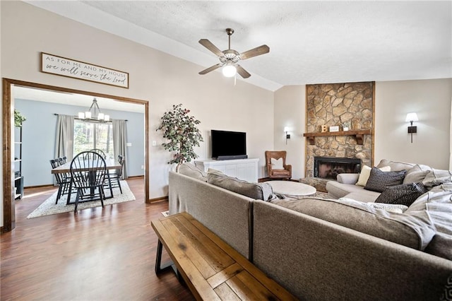 living room featuring baseboards, lofted ceiling, a stone fireplace, ceiling fan with notable chandelier, and dark wood-style floors