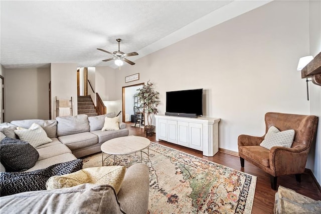 living area with a ceiling fan, a textured ceiling, wood finished floors, baseboards, and stairs