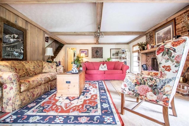 living room featuring wooden walls, carpet flooring, stairway, a brick fireplace, and beam ceiling