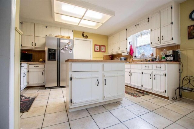 kitchen featuring light tile patterned floors, stainless steel refrigerator with ice dispenser, kitchen peninsula, and white cabinetry