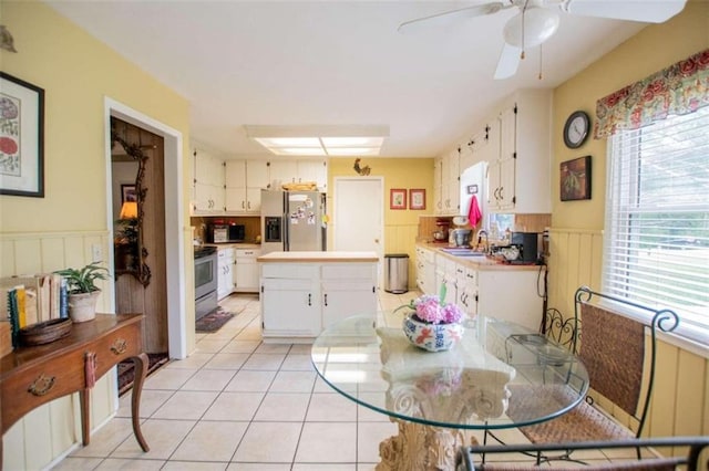 dining space with ceiling fan, wainscoting, and light tile patterned flooring