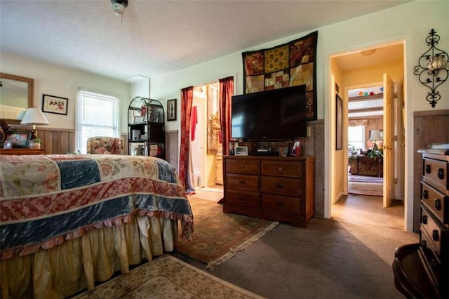 carpeted bedroom featuring a wainscoted wall, wooden walls, and ensuite bathroom