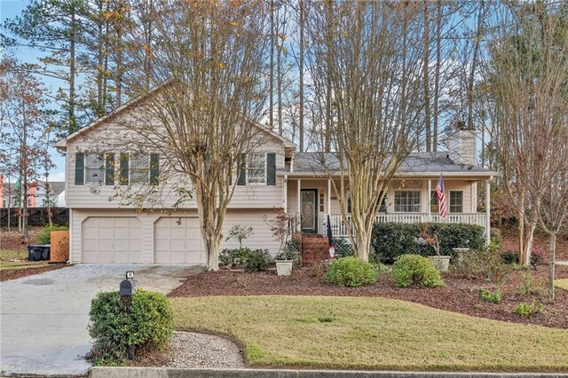 split level home with covered porch, a garage, and a front lawn