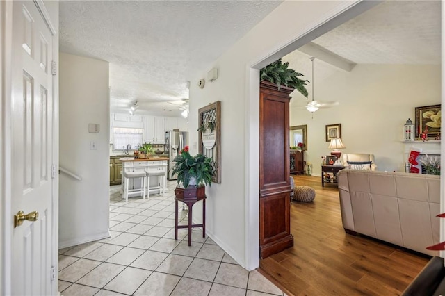 corridor featuring a textured ceiling, light wood-type flooring, vaulted ceiling with beams, and sink