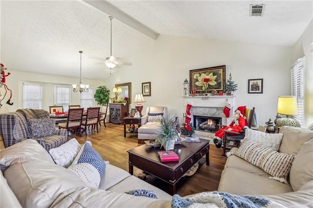 living room with ceiling fan with notable chandelier, beam ceiling, high vaulted ceiling, a premium fireplace, and hardwood / wood-style floors