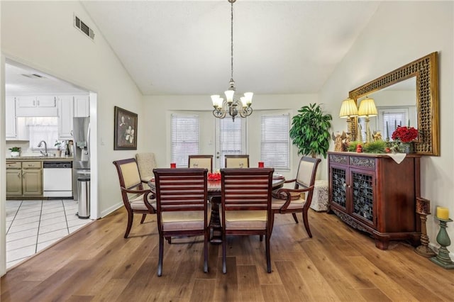 dining room with an inviting chandelier, lofted ceiling, sink, and light hardwood / wood-style flooring