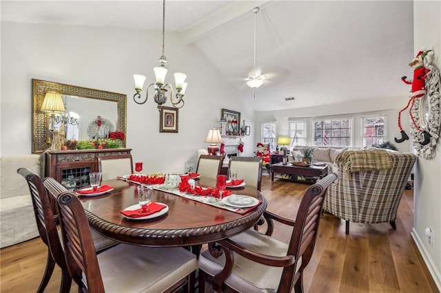 dining space with ceiling fan with notable chandelier, wood-type flooring, and vaulted ceiling with beams