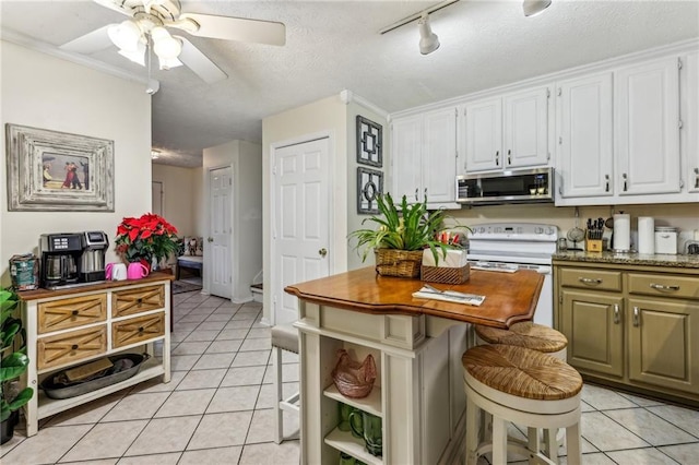 kitchen with ceiling fan, light tile patterned floors, white range with electric stovetop, a kitchen bar, and white cabinets