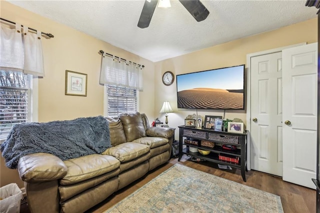 living room featuring ceiling fan, dark wood-type flooring, and a textured ceiling