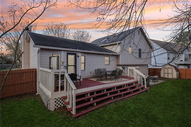 back house at dusk featuring a shed, a deck, and a lawn