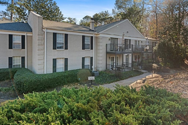 view of front facade featuring a chimney, brick siding, a patio, and roof with shingles