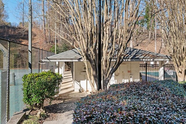 view of side of home featuring brick siding, fence, and roof with shingles