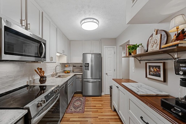 kitchen featuring open shelves, light wood-style floors, appliances with stainless steel finishes, backsplash, and a sink