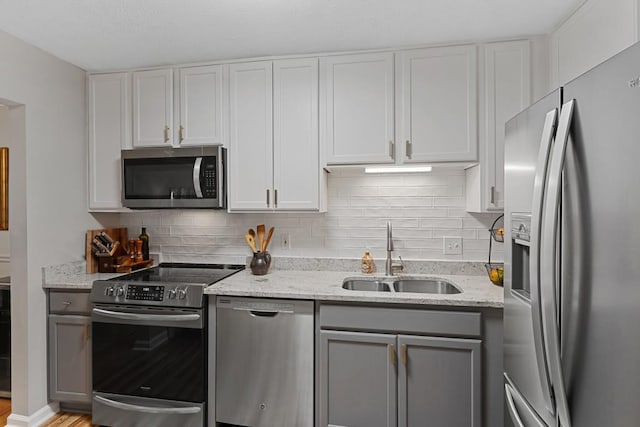 kitchen with tasteful backsplash, a sink, appliances with stainless steel finishes, light stone countertops, and gray cabinets