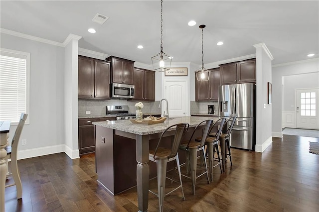 kitchen with a kitchen island with sink, hanging light fixtures, crown molding, dark brown cabinets, and stainless steel appliances