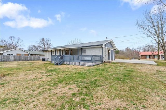 view of front of property featuring brick siding, covered porch, central AC, fence, and a front lawn