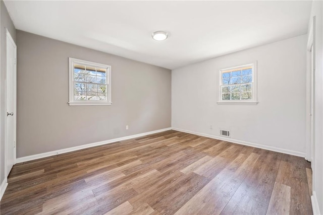 unfurnished bedroom with multiple windows, wood finished floors, visible vents, and baseboards