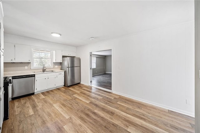 kitchen featuring light wood-style flooring, stainless steel appliances, a sink, white cabinets, and light countertops