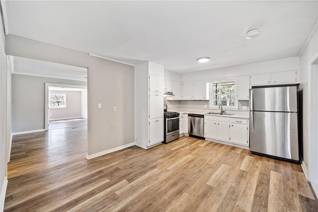 kitchen featuring under cabinet range hood, stainless steel appliances, a sink, light countertops, and light wood finished floors