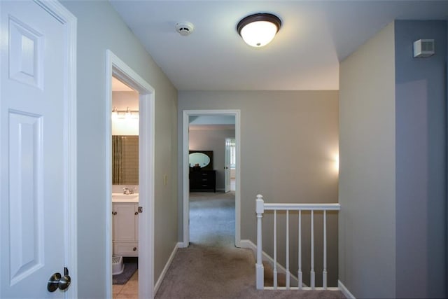 corridor with a sink, light colored carpet, an upstairs landing, and baseboards
