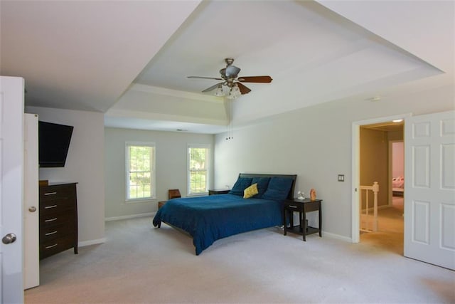 bedroom with a raised ceiling, light carpet, baseboards, and a ceiling fan
